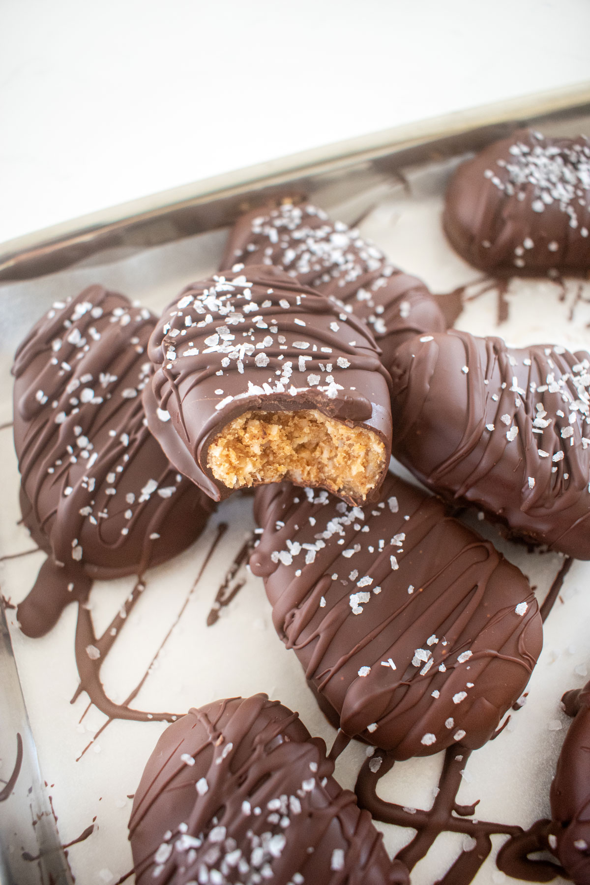 dark chocolate coconut almond butter eggs with flaky sea salt on a baking sheet, one with a bite taken out.
