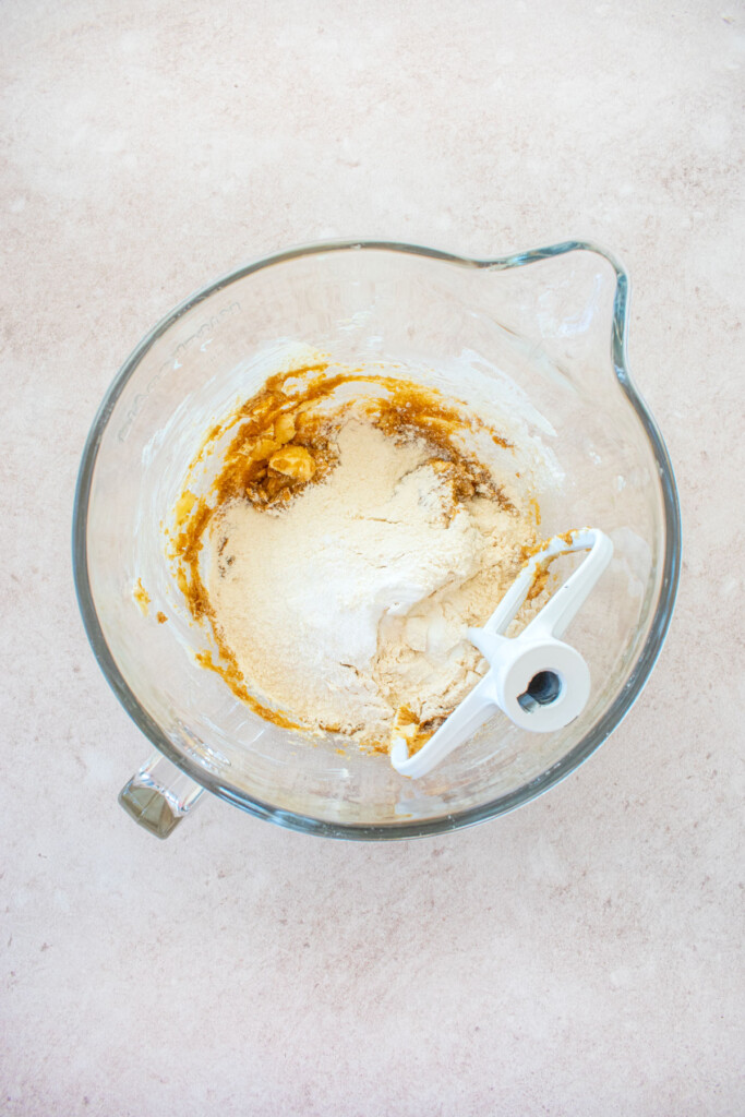 ingredients for easter banana blondies in a glass stand mixing bowl on a pink counter.