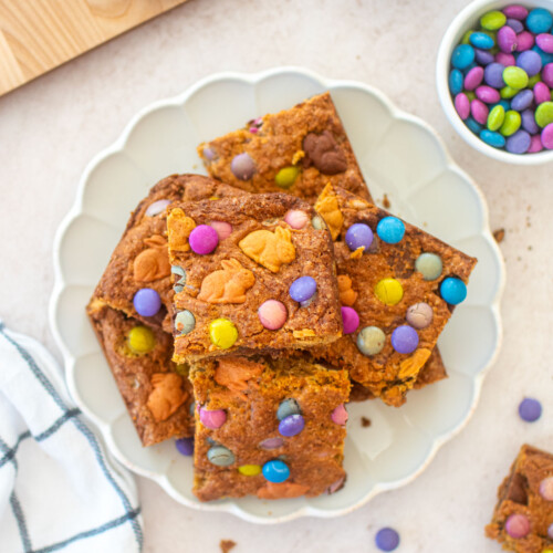 easter banana blondies cut into squares on a ruffle plate on a pink counter.