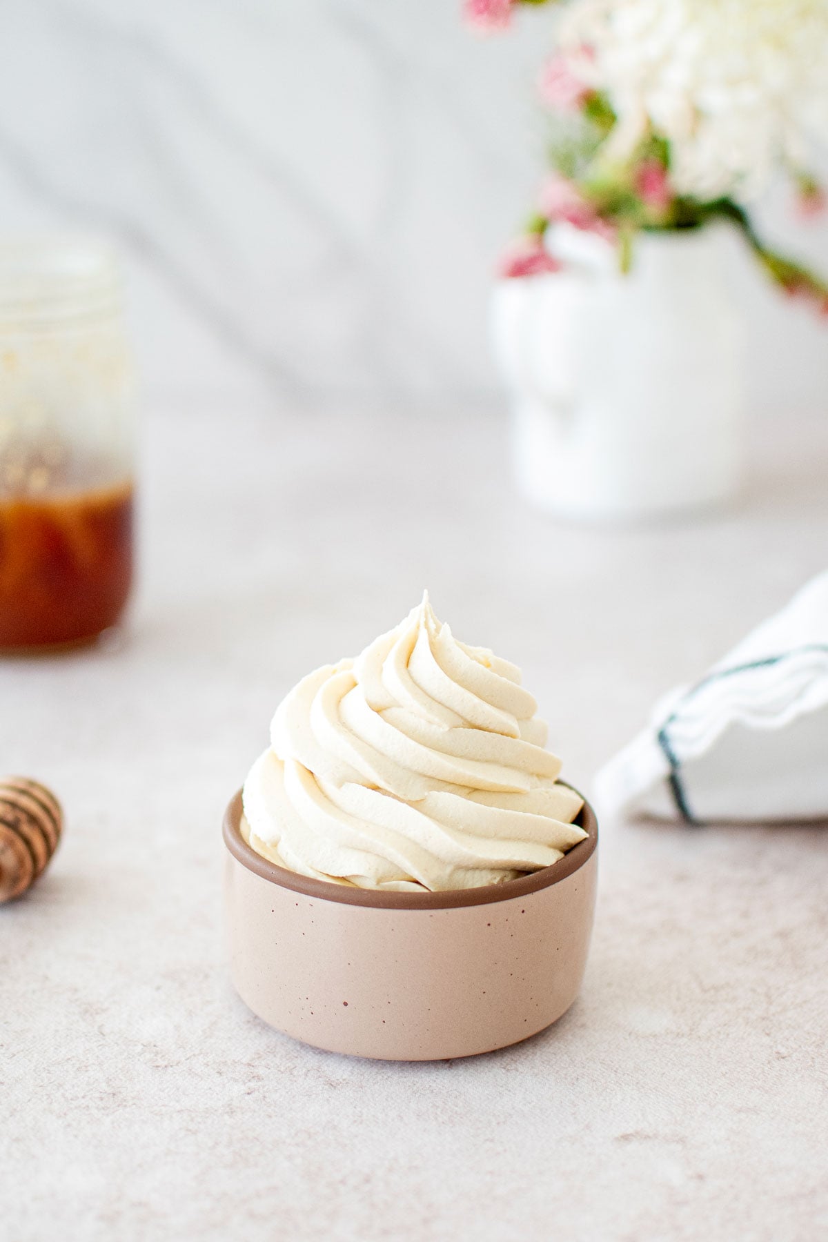 small bowl with honey buttercream swirled in it on a table with fresh flowers.