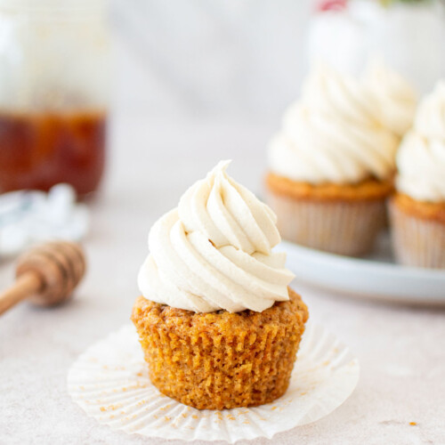 carrot cupcake with the wrapper unpeeled with honey buttercream on top sitting on a table with fresh flowers.