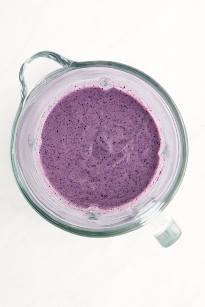frozen blueberry mixture in a glass blender on a white marble countertop.