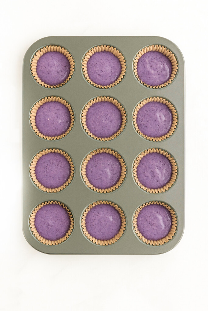 blueberry cheesecake for dogs filling in a cupcake pan on a white marble countertop.