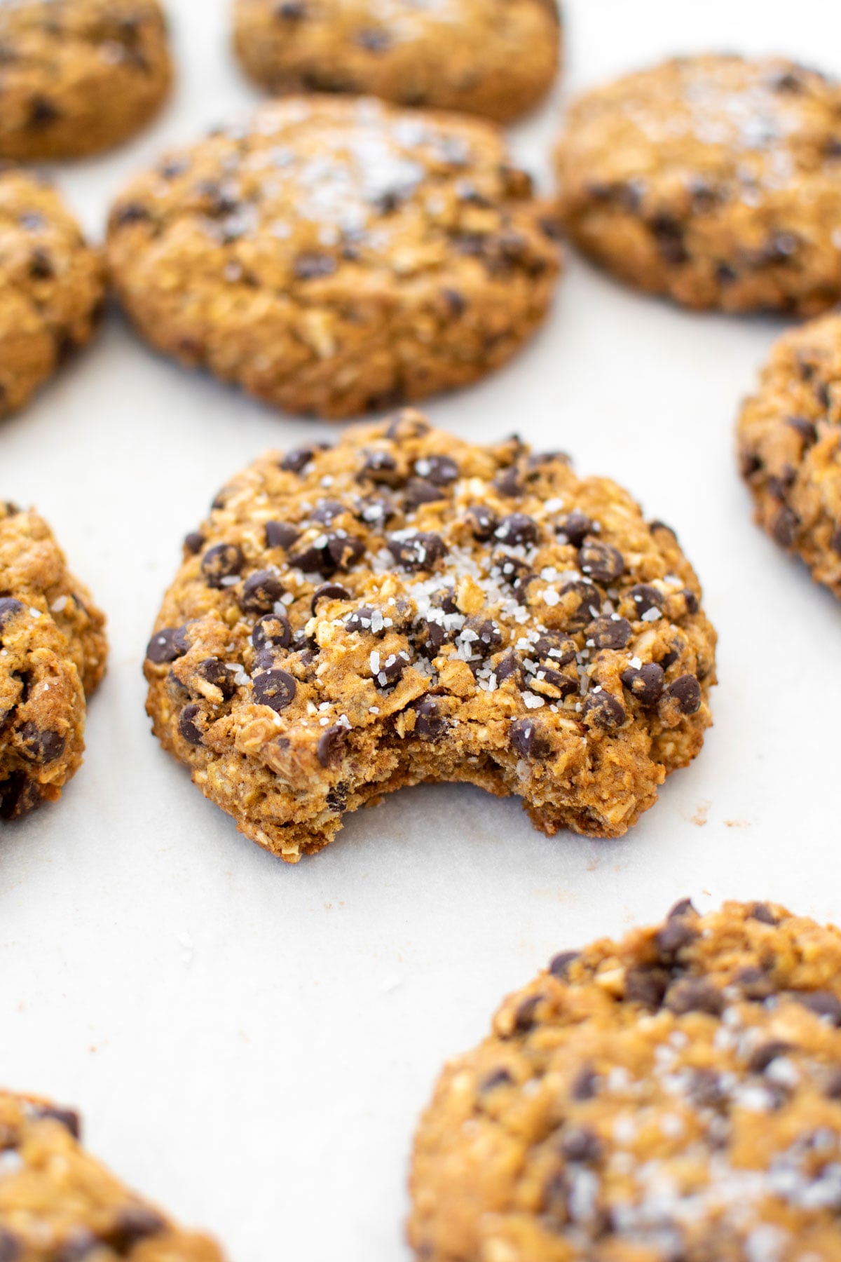 pumpkin oatmeal chocolate chip cookies on a baking sheet, one with a bite taken out.
