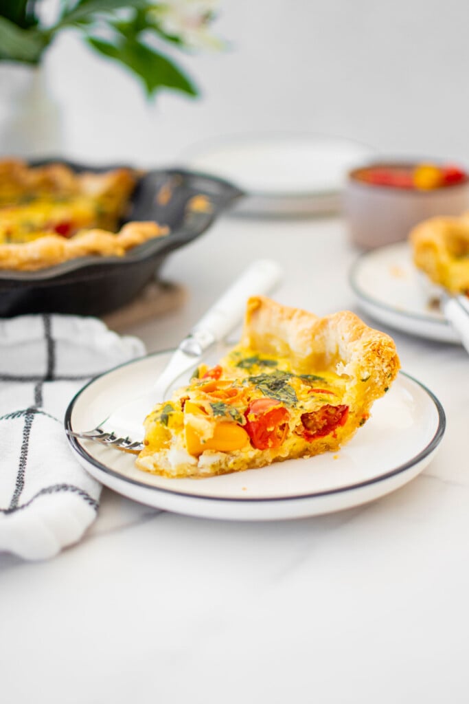 slice of tomato basil quiche with bone broth on plate on a white marble countertop.