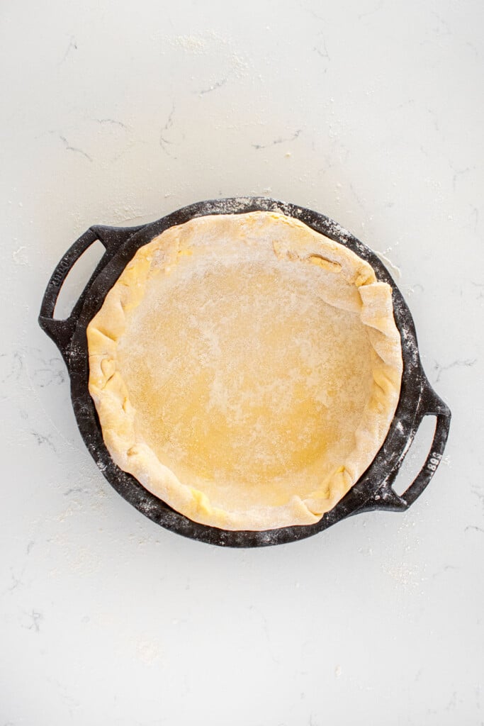 pie crust in a cast iron pie pan on a white marble countertop.