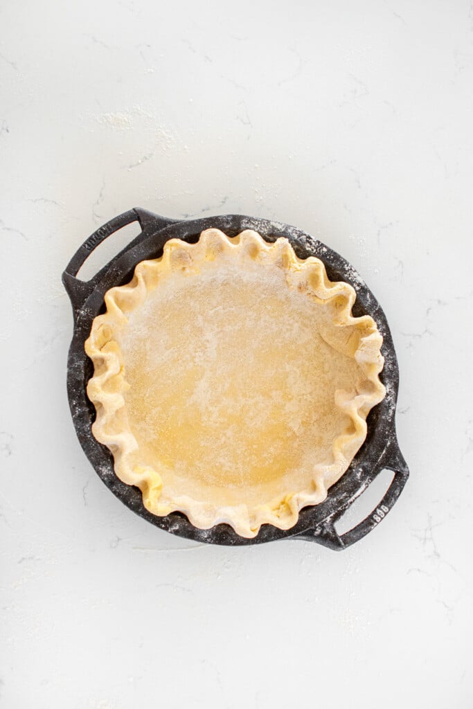 pie crust with fluted edges in a cast iron pie pan on a white marble countertop.