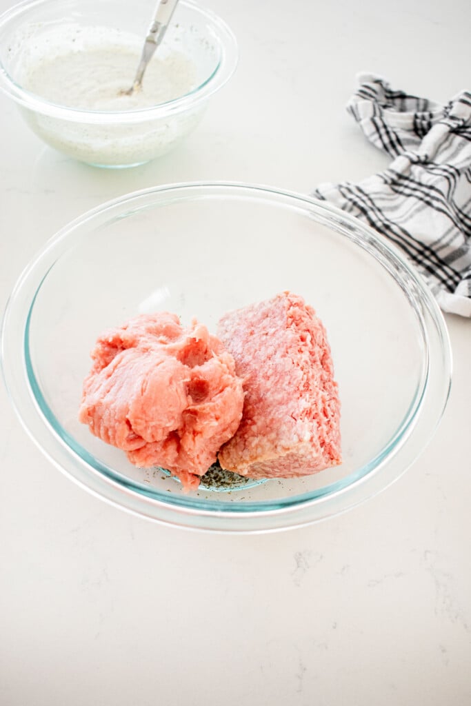 ground turkey ground lamb and in a glass mixing bowl with spices on a marble counter.