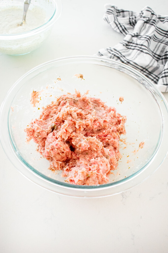 ground turkey ground lamb mixed together with spices in a glass mixing bowl on a marble counter.