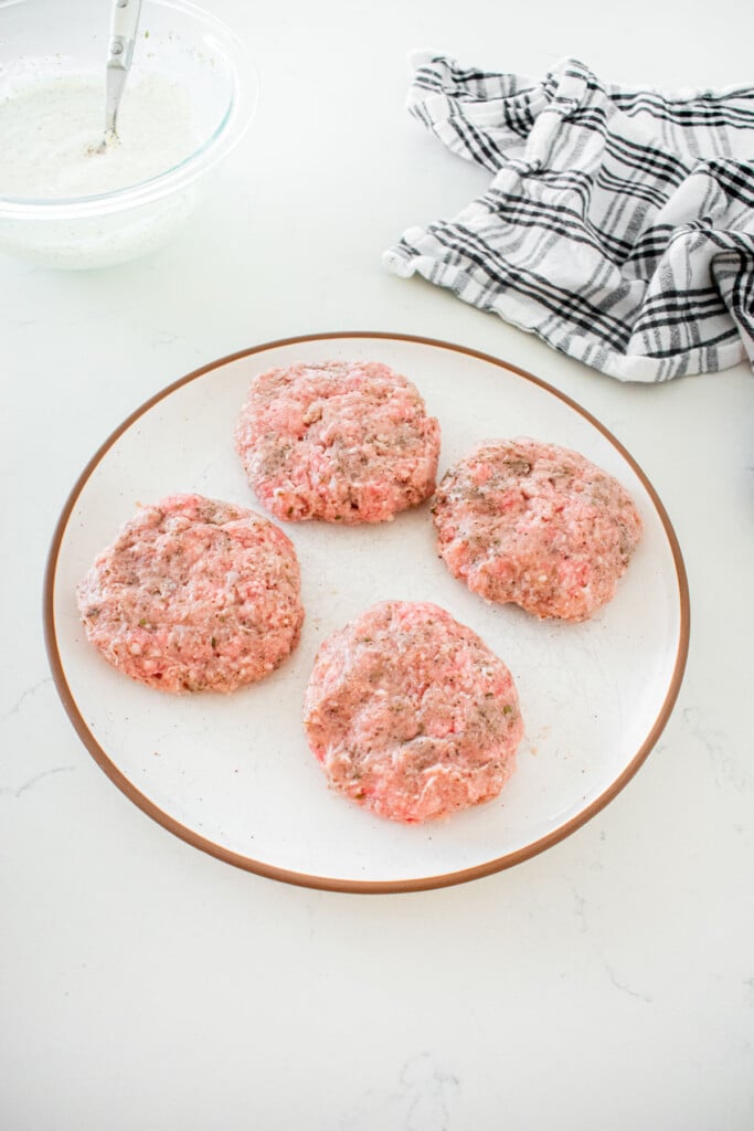 plate with four ground lamb and turkey burger patties formed on a marble counter.