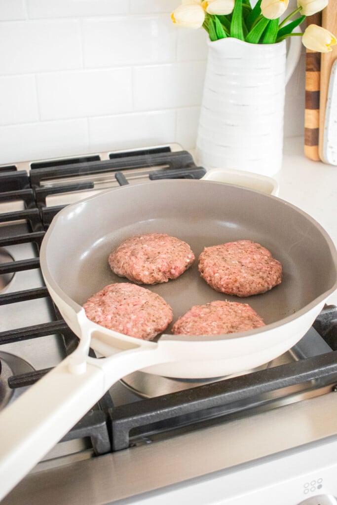 large skillet with turkey and lamb burgers being cooked on the stoveop.