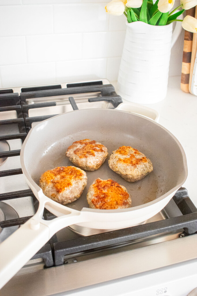 large skillet with turkey and lamb burgers being cooked on the stoveop.