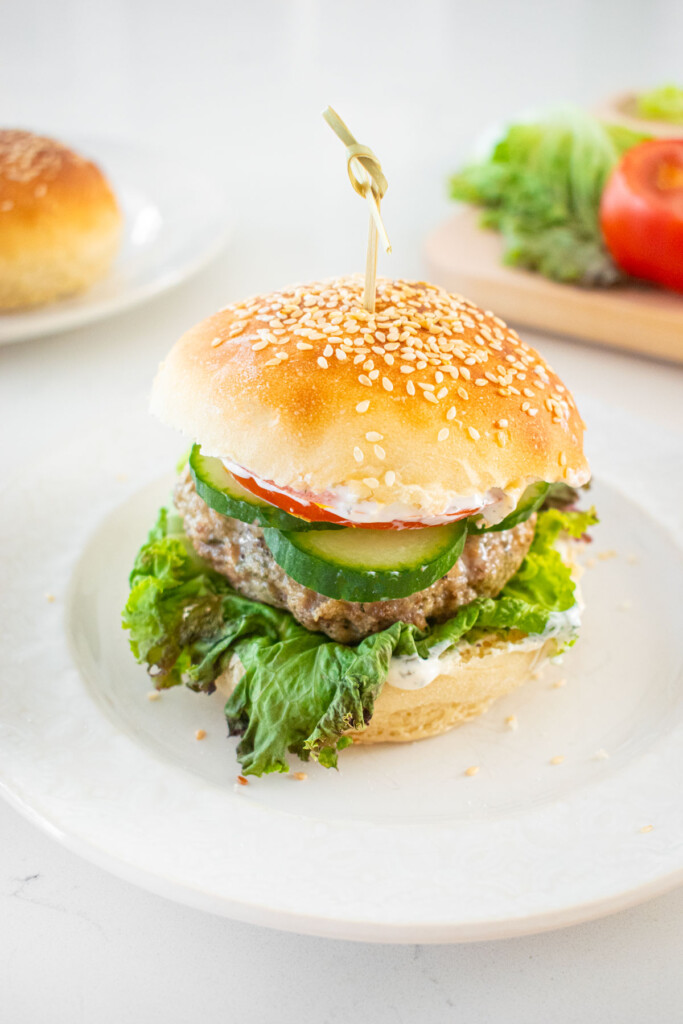 turkey and lamb burger with dill sauce on a plate on a marble counter.