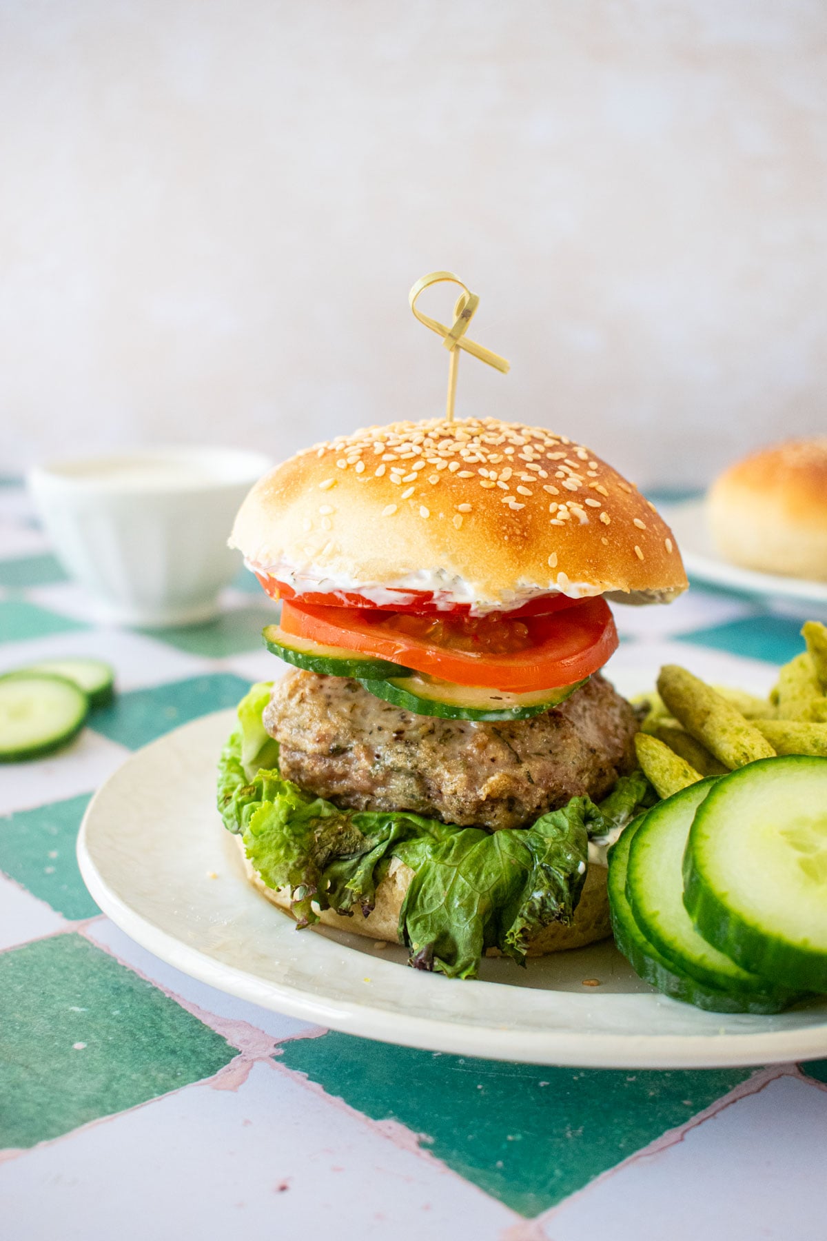 turkey lamb burger with dill sauce on on plate on a green tile table.