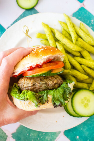 turkey lamb burger with dill sauce being grabbed with a hand on on plate on a green tile table.