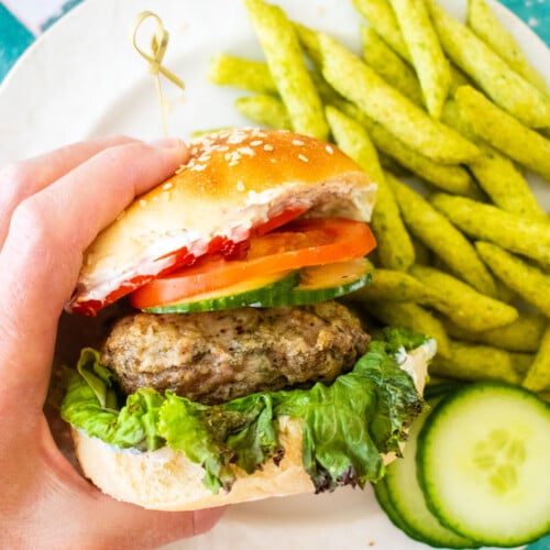 turkey lamb burger with dill sauce being grabbed with a hand on on plate on a green tile table.