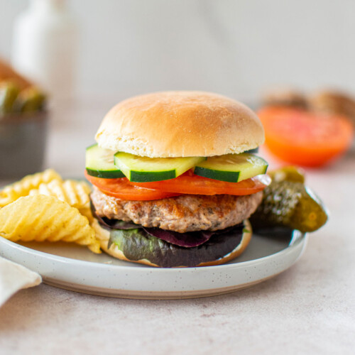 turkey lamb burger with dill sauce on a plate with chips and pickles.