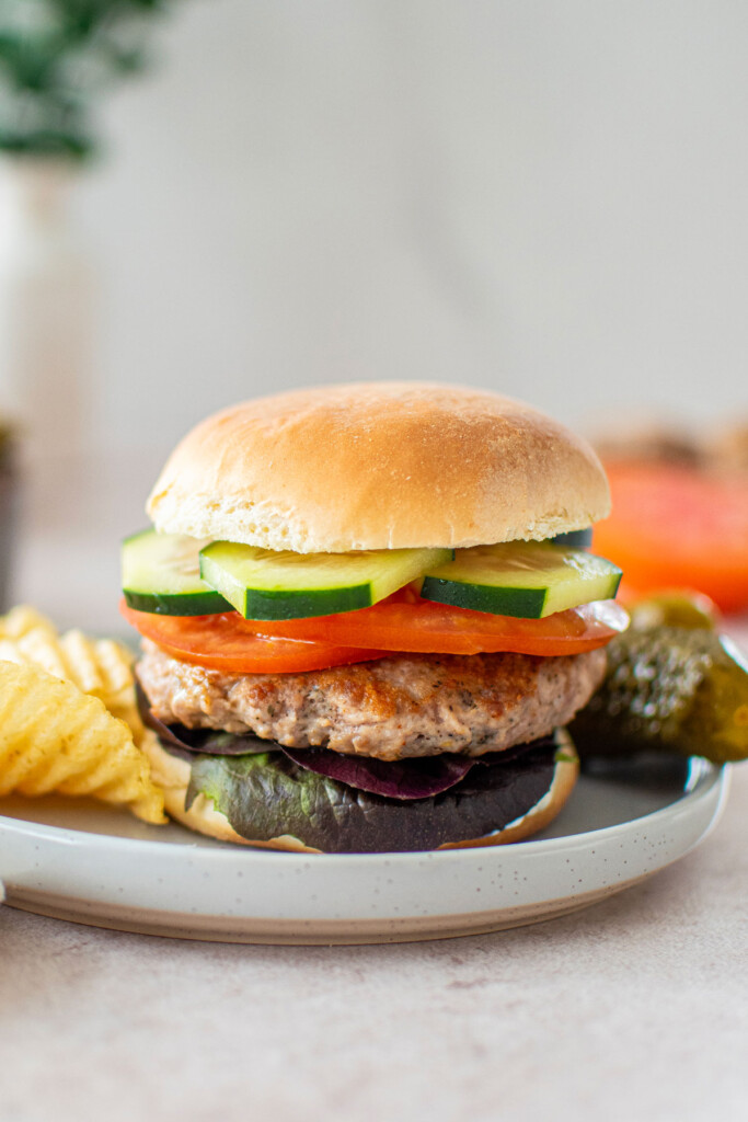 turkey lamb burger with dill sauce on a plate with chips and pickles.