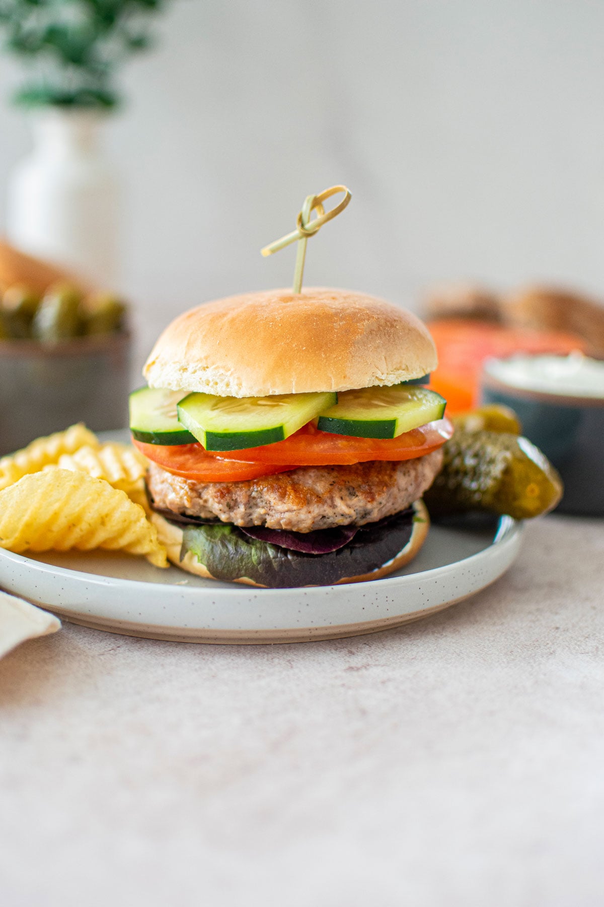 turkey lamb burger with dill sauce on a plate with chips and pickles.