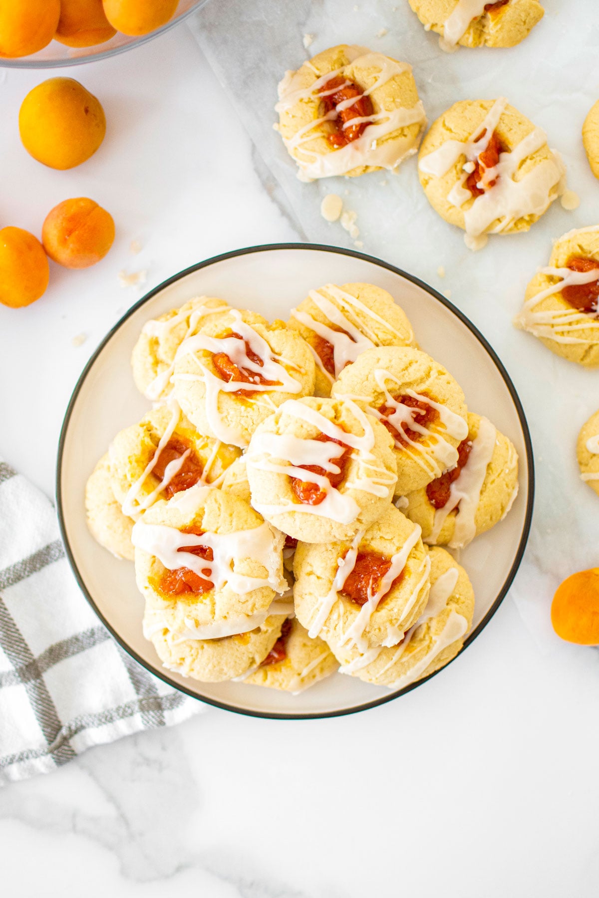 plate of apricot jam thumbprint cookies with glaze on a plate on a marble counter.