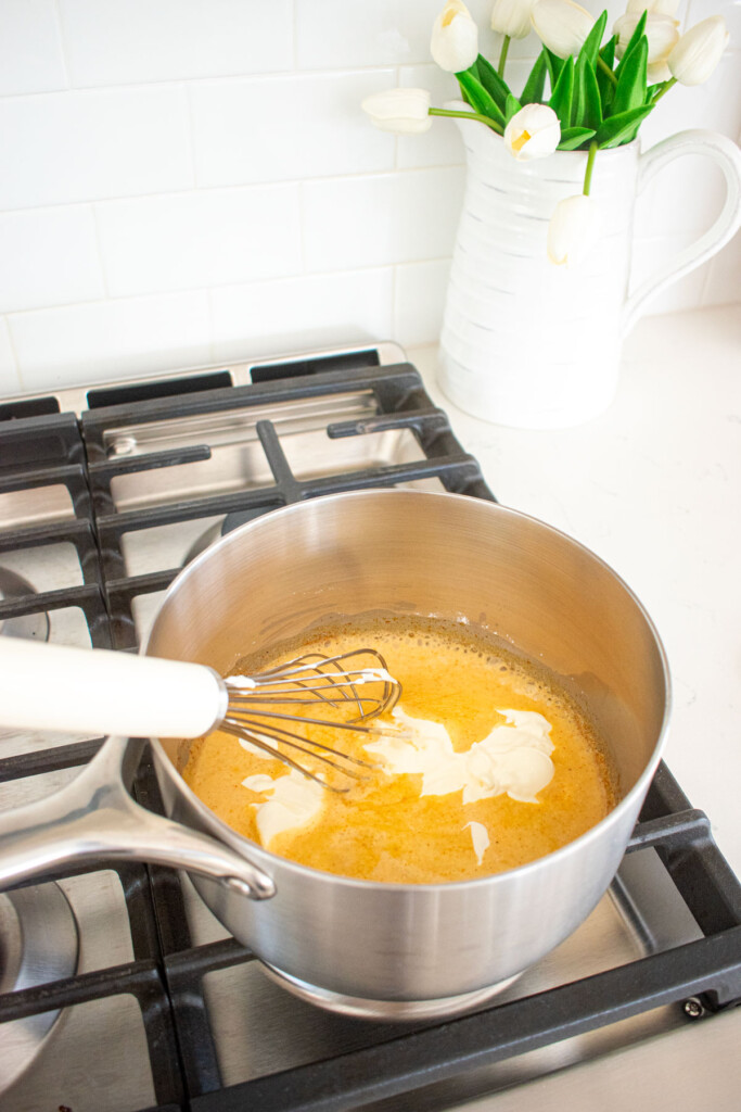sour cream being added to bone broth queso dip being stirred with a whisk in a pot on the stovetop.