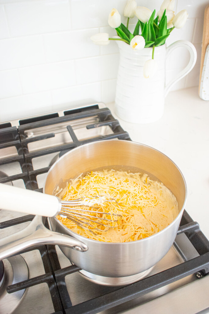 cheese being added to bone broth queso dip being stirred with a whisk in a pot on the stovetop.