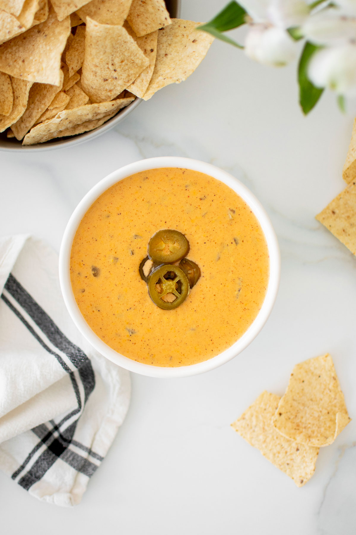 bone broth queso dip in a white bowl on a marble countertop with a bowl of chips.