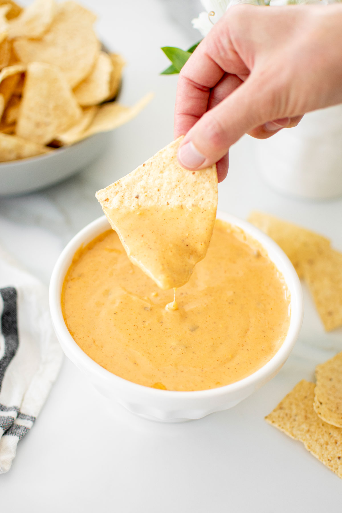 corn chip being dipped into a bowl of bone broth queso dip on a white marble top.