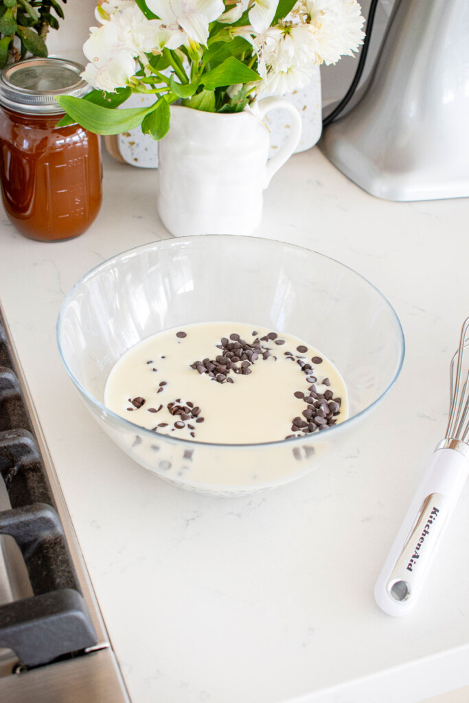 cream and dark chocolate chips in a glass mixing bowl on a white marble counter.