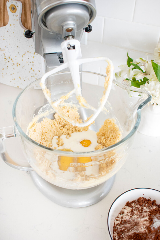 ingredients for chocolate pound cake in a glass stand mixing bowl with flour mixture in a bowl next to it.
