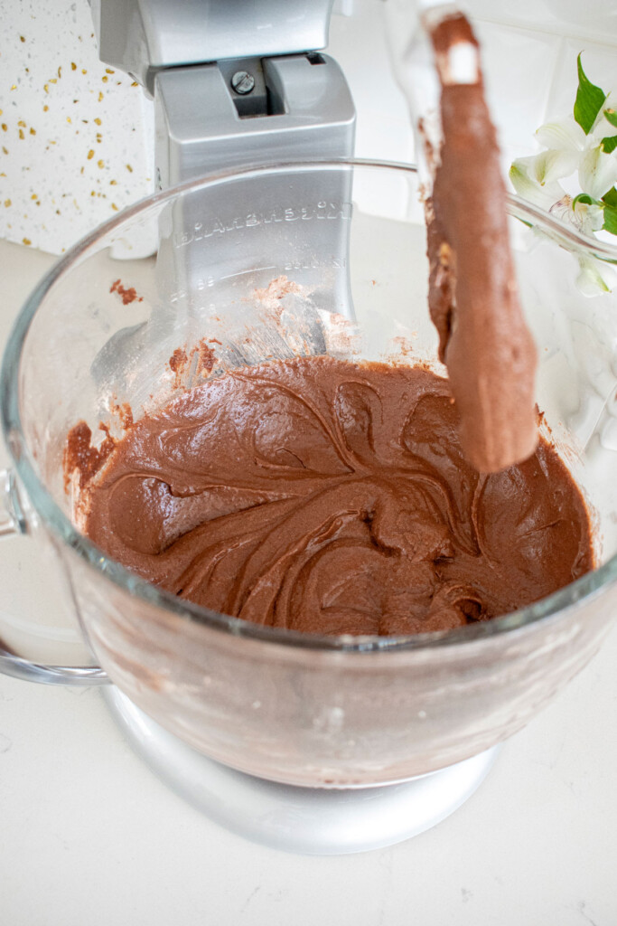 chocolate pound cake batter in a glass mixing bowl on a white marble counter.