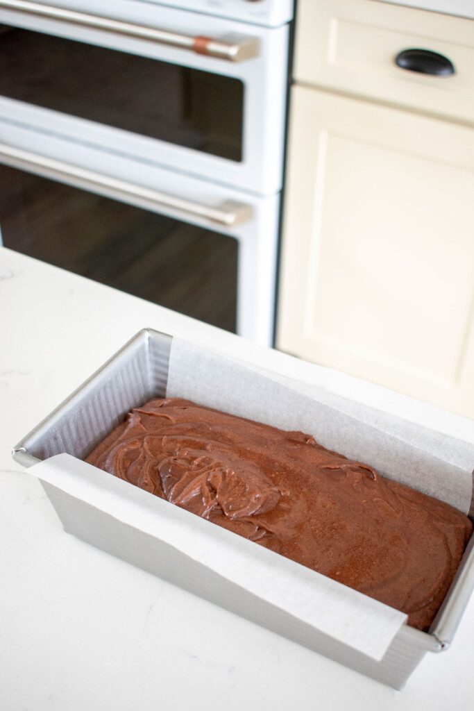 chocolate pound cake batter in a loaf pan on a white marble counter.
