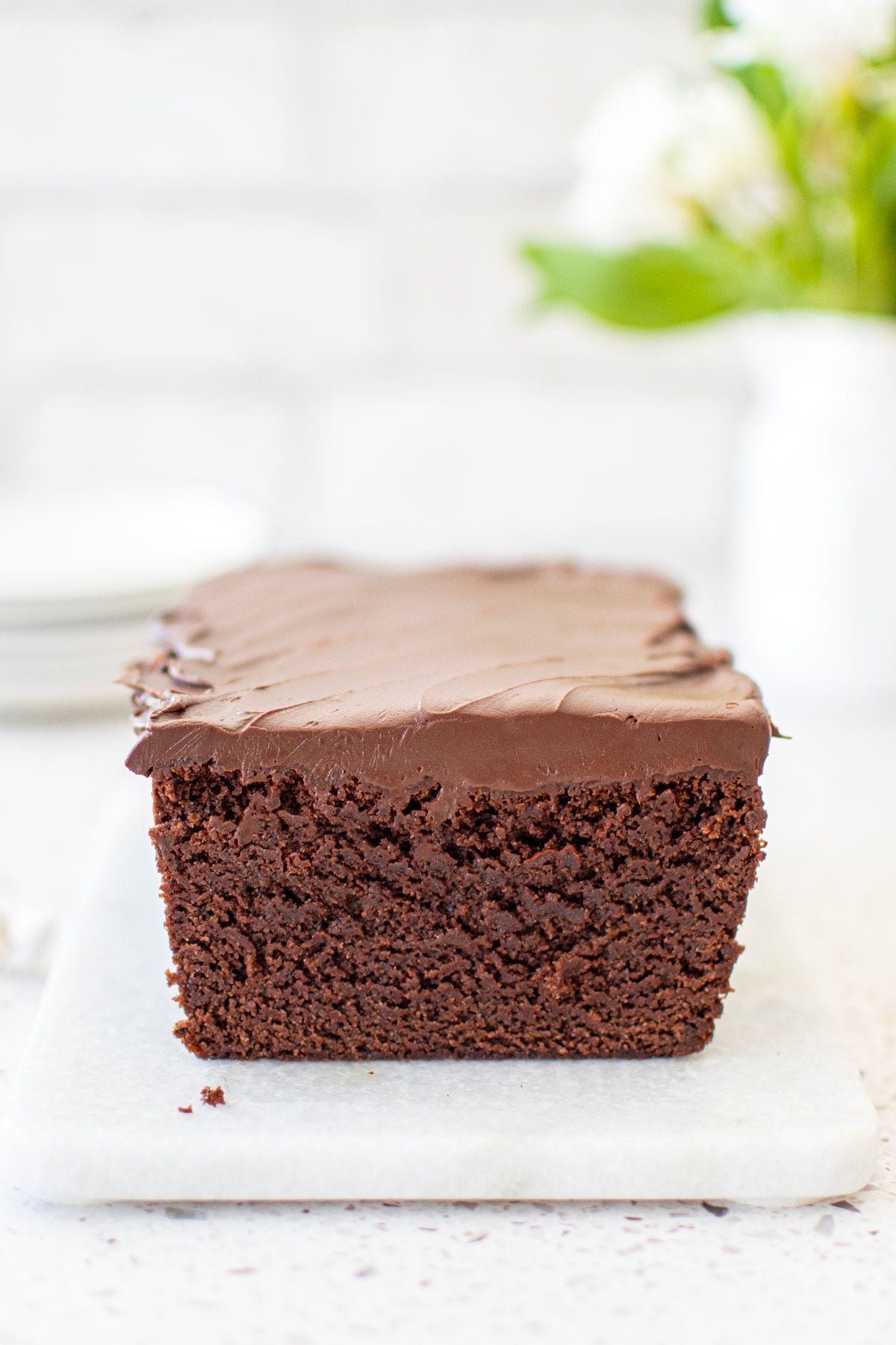 chocolate pound cake with chocolate ganache frosting on a white marble serving board with fresh flowers.