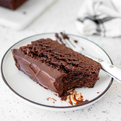 chocolate pound cake with chocolate ganache frosting on a plate with a bite taken out on a marble counter.