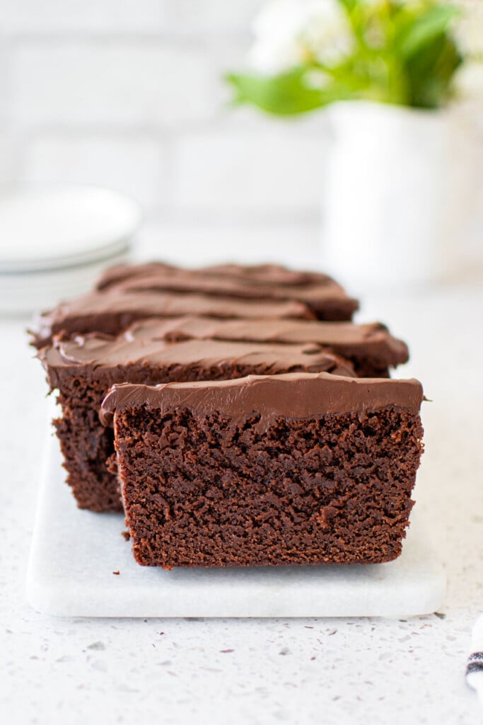 chocolate pound cake with chocolate ganache frosting sliced on a white marble serving board with fresh flowers.