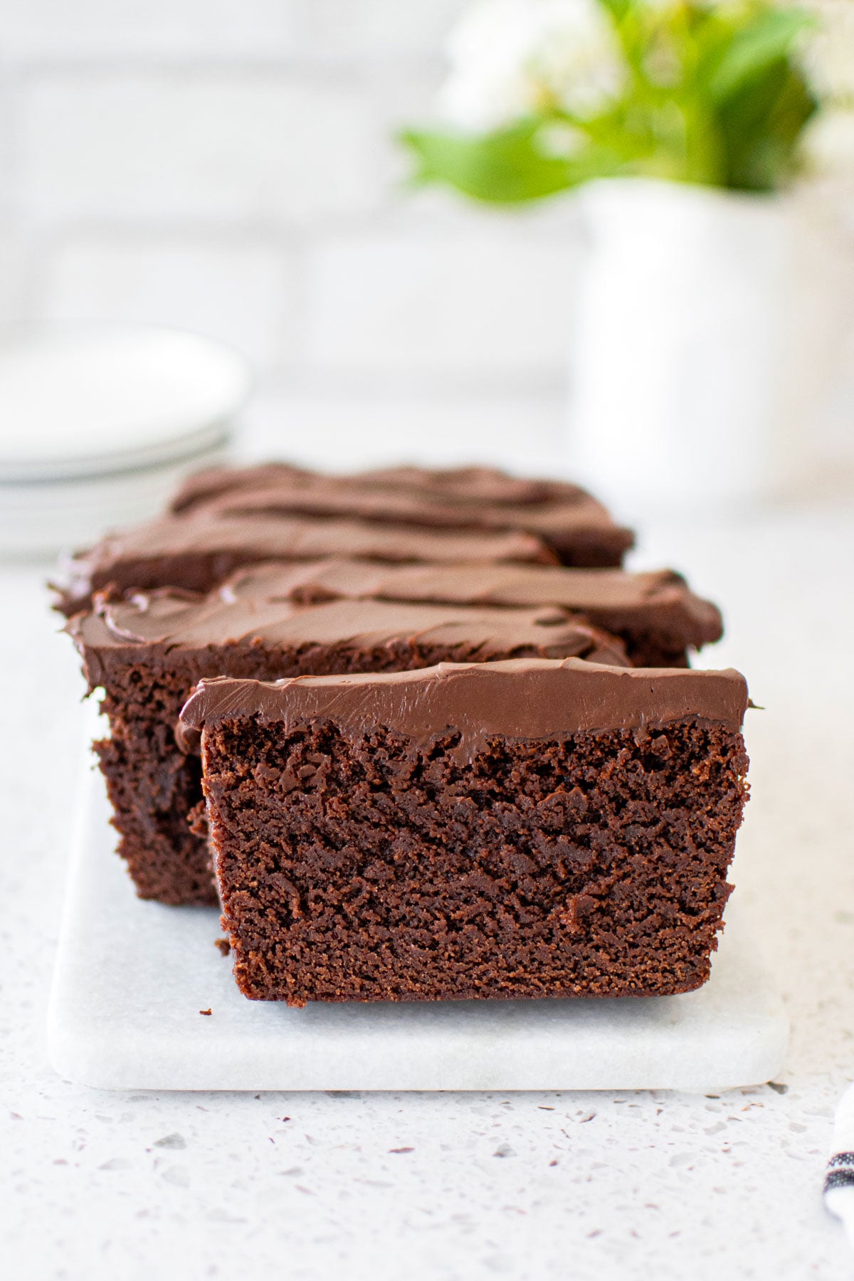 chocolate pound cake with chocolate ganache frosting sliced on a white marble serving board with fresh flowers.