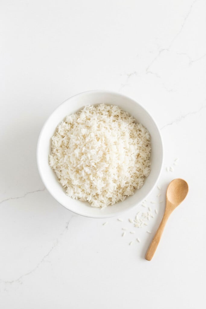 white rice in a white bowl on a white marble counter with a wooden spoon.