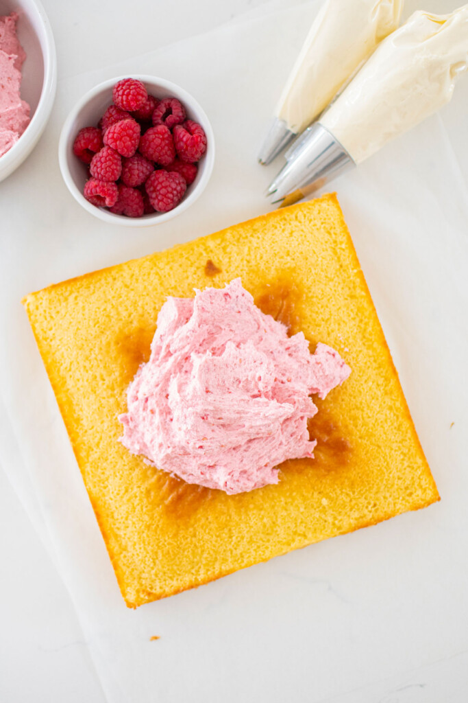 square lemon snack cake with fresh raspberry frosting on top on a marble counter.