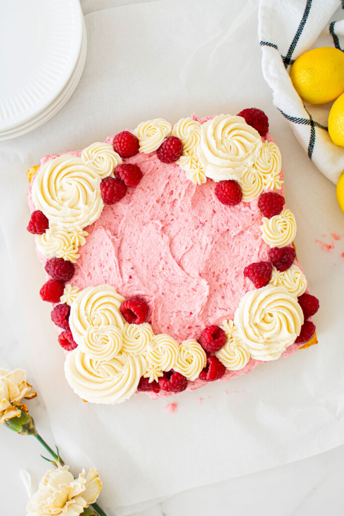 square raspberry lemon snack cake with buttercream roses and fresh raspberries on top on a marble counter.