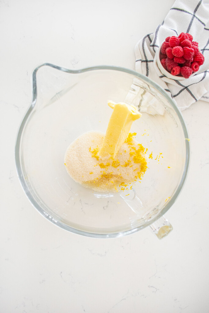 butter, cane sugar, lemon zest and lemon flavor in a glass mixing bowl on a marble counter.