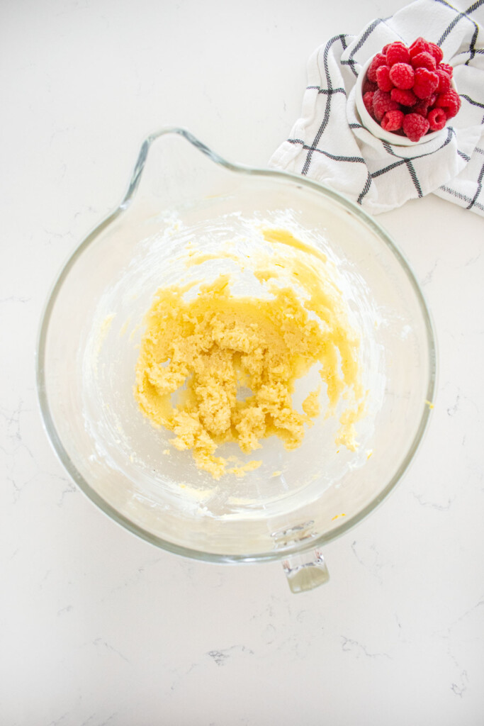 creamed butter and cane sugar in a glass mixing bowl on a white marble counter.