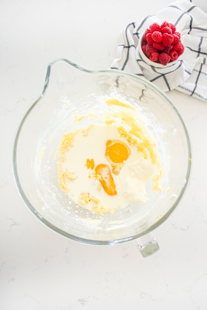 creamed butter and cane sugar with eggs, milk and sour cream in a glass mixing bowl on a marble counter.