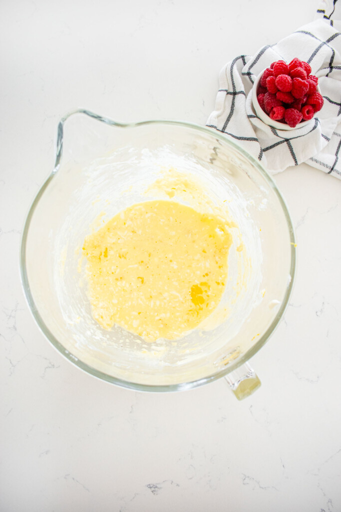 wet ingredients mixed into butter and sugar mixture in a glass mixing bowl on a marble counter.
