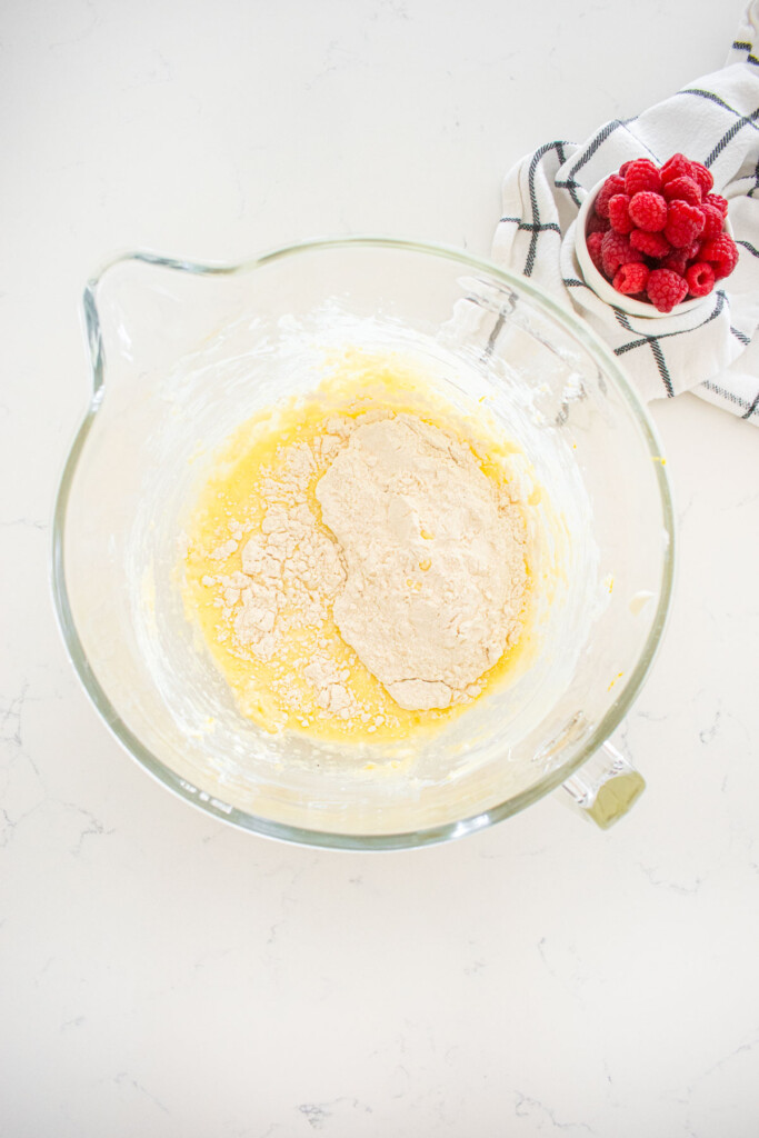 dry ingredients added to wet ingredients for a lemon cake in a glass mixing bowl on a marble counter.
