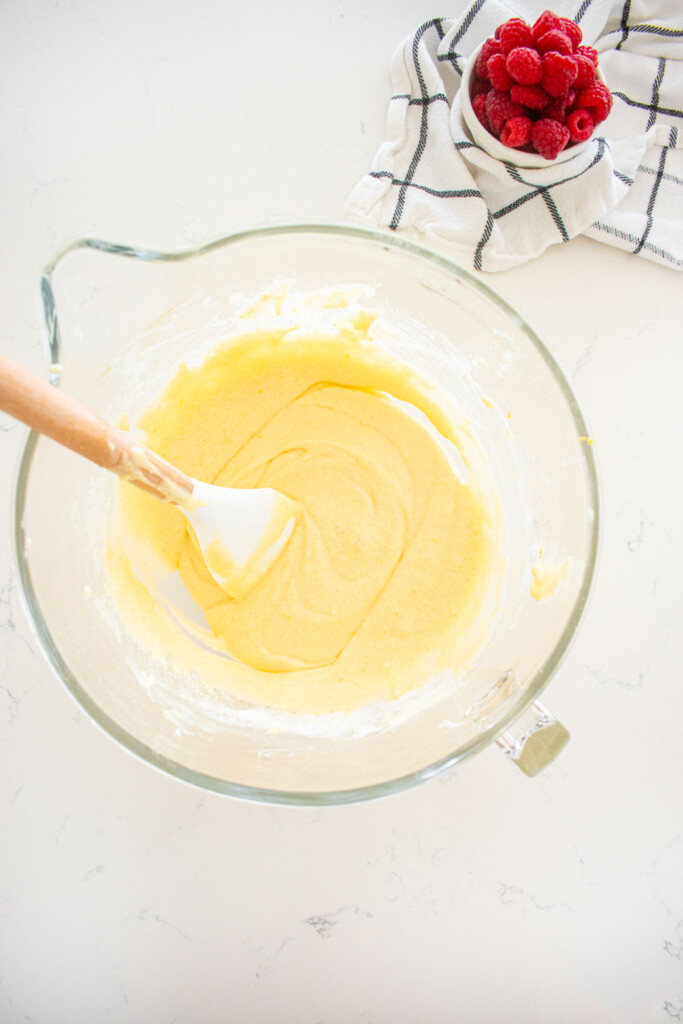 lemon cake batter in a glass mixing bowl on a white marble counter.