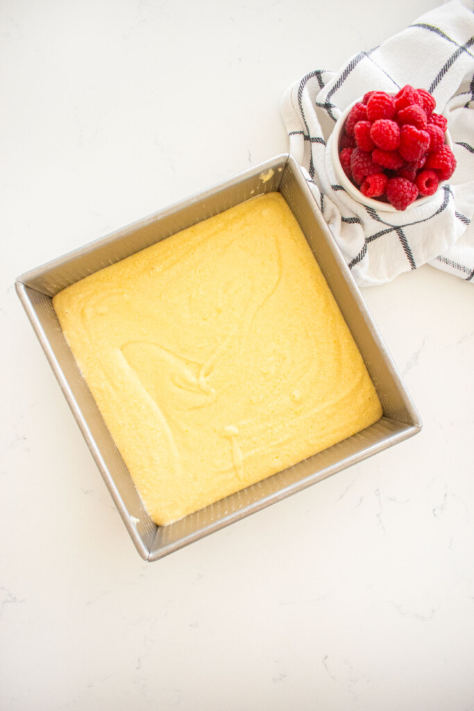 square cake pan with lemon cake batter spread evenly in it on a marble counter.