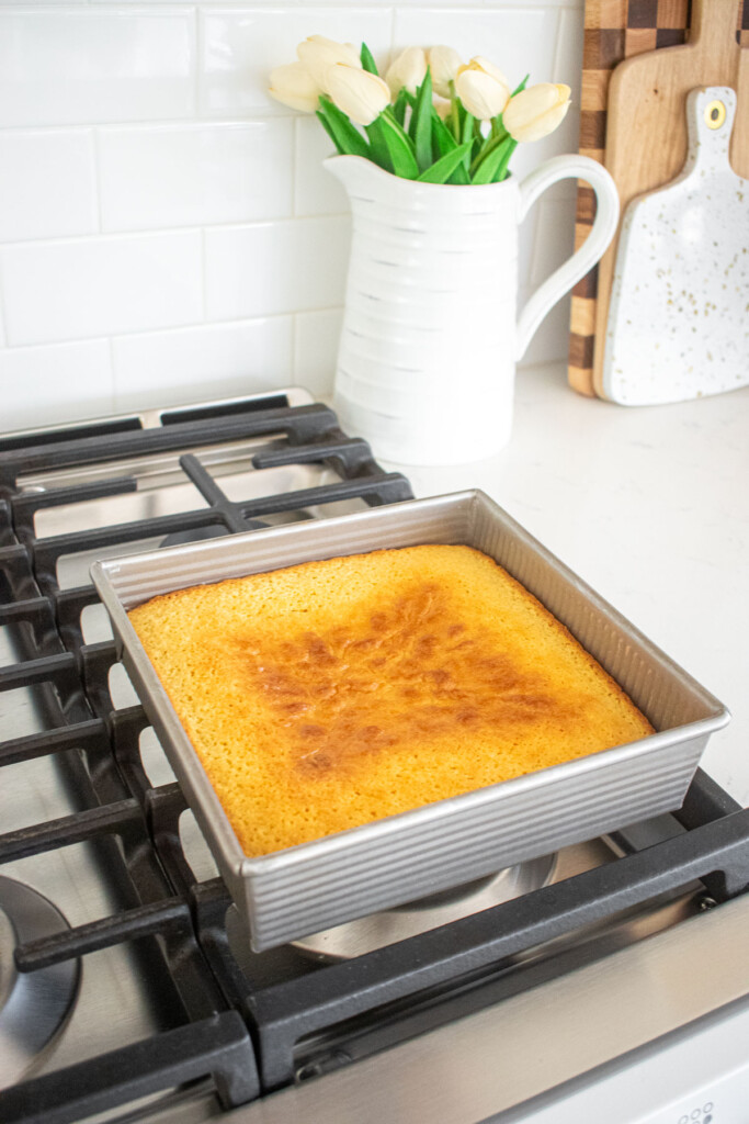 baked lemon cake in a square cake pan cooling on top of an oven.