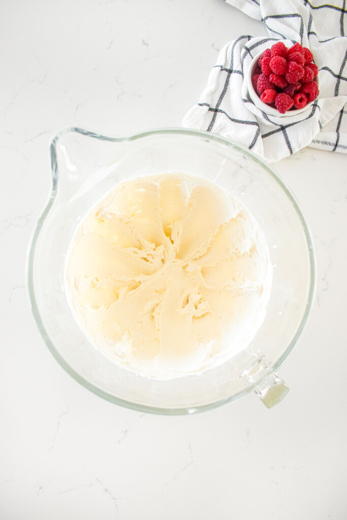 white buttercream frosting in a glass mixing bowl on a marble counter.