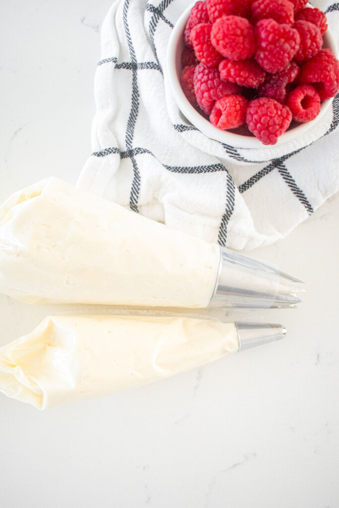 two piping bags with white frosting and decorating tips on a a white marble counter.