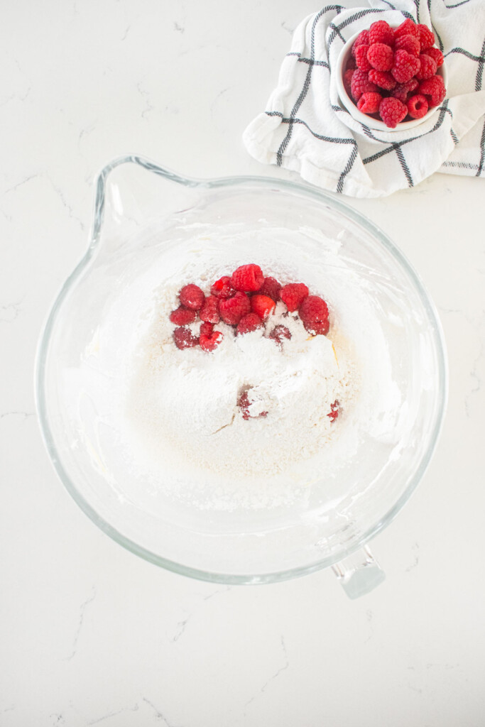 ingredients for raspberry buttercream frosting in a glass mixing bowl on a marble counter.